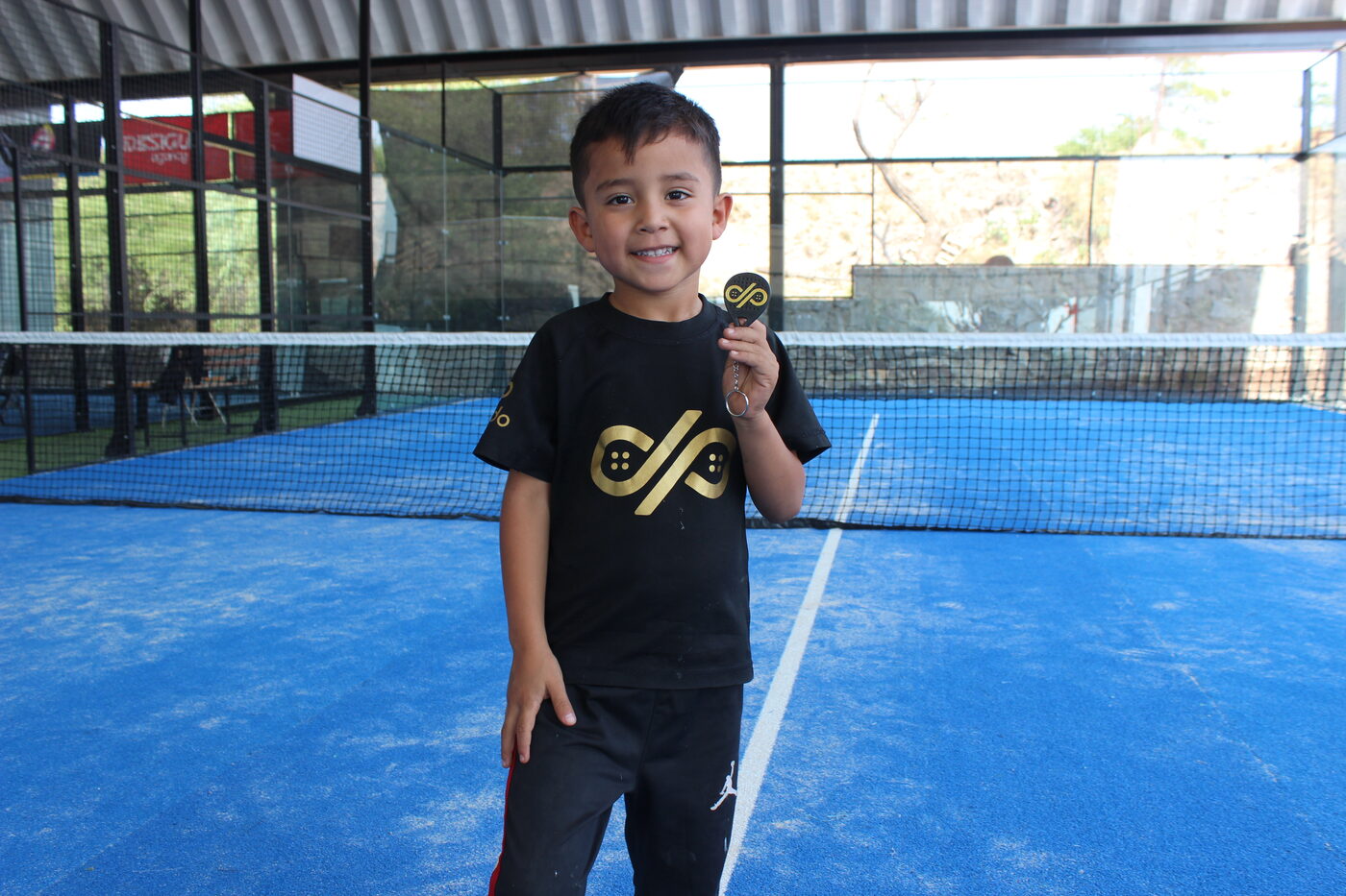 Niño con playera de Dorado en la cancha de pádel